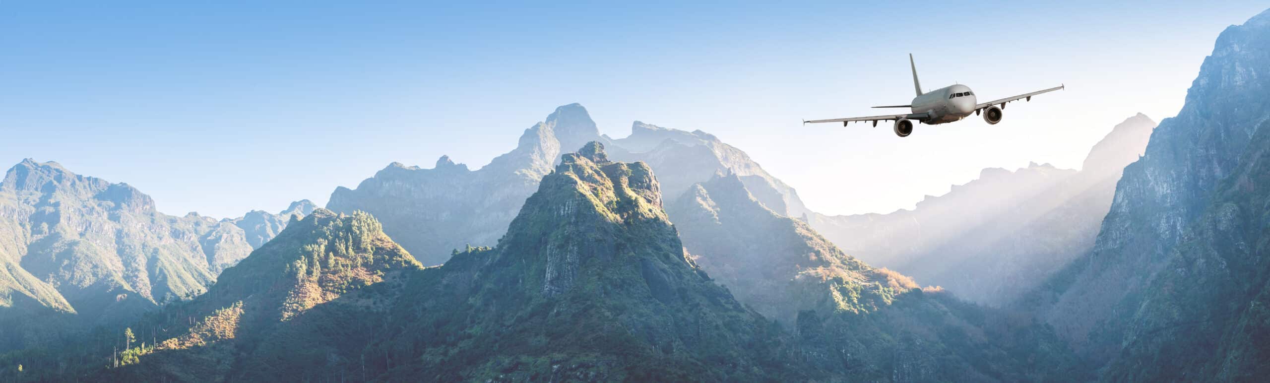 Airplane is flying over mountains in fog at sunset in summer. Landscape with passenger airplane, hills in low clouds, blue sky. White aircraft. Business travel.